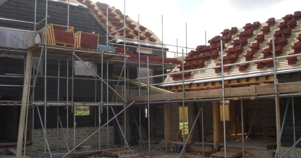 House under construction showing larch cladding on left and roof being tiled on right