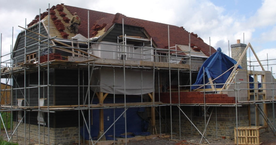 House under construction, larch cladding, man laying tiles